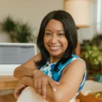 A smiling businesswoman sits confidently at her desk in a modern office setting.